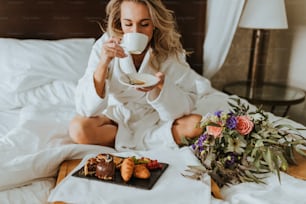 ベッドに座ってコーヒーを飲む女性
