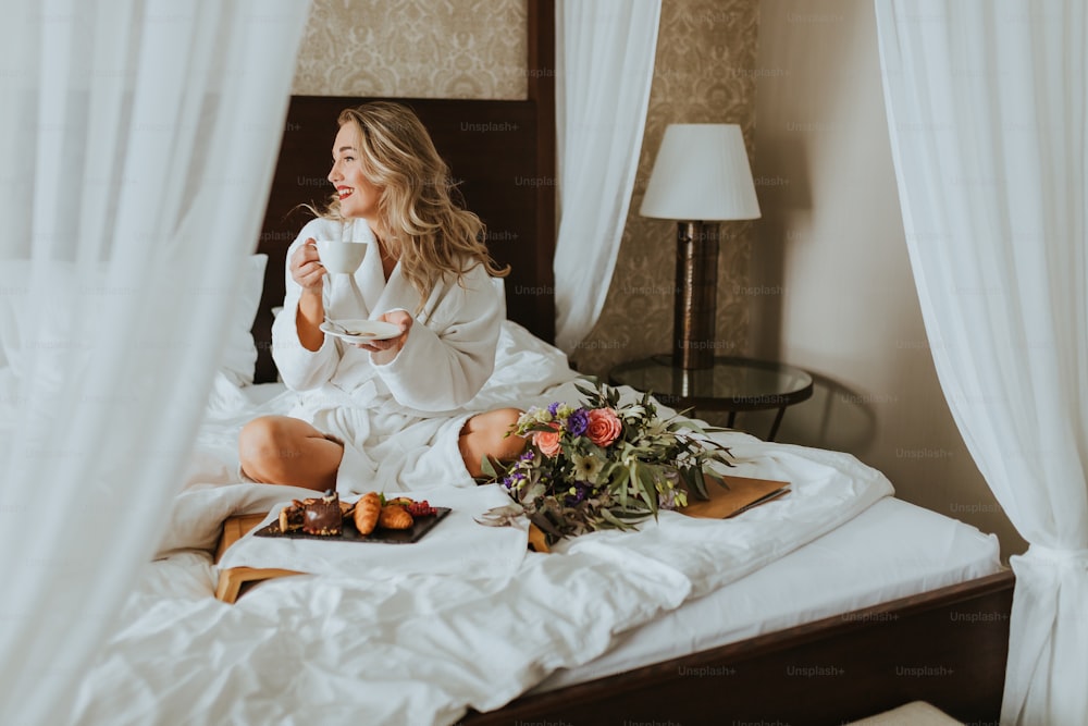 uma mulher sentada em uma cama bebendo uma xícara de café