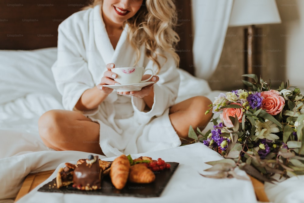 Une femme assise sur un lit tenant une tasse de café
