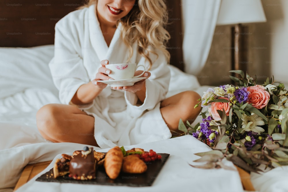 a woman sitting on a bed holding a cup of coffee