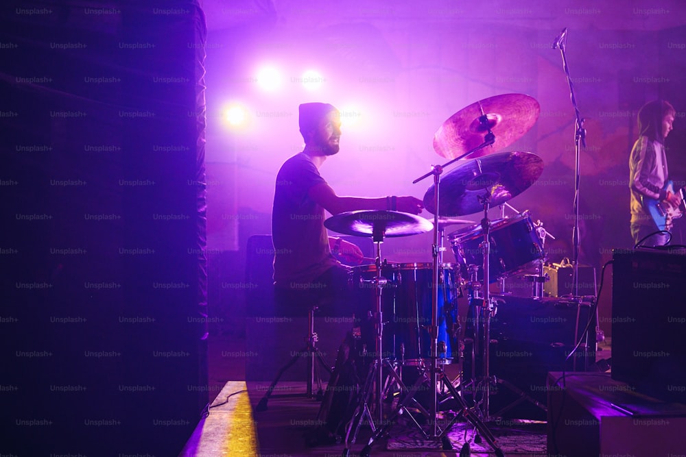 보라색 불빛 앞에서 드럼을 연주하는 남자