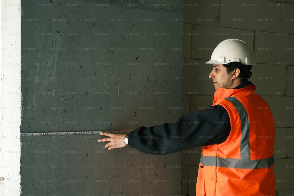 a man in an orange safety vest and hard hat measuring a wall