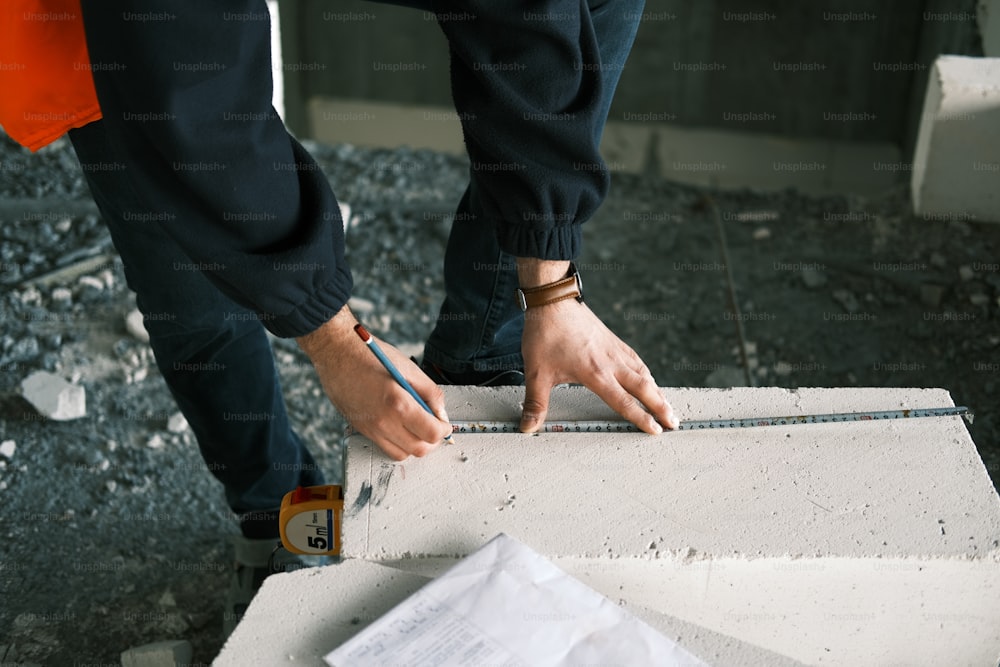 uma pessoa segurando um lápis e medindo um pedaço de concreto