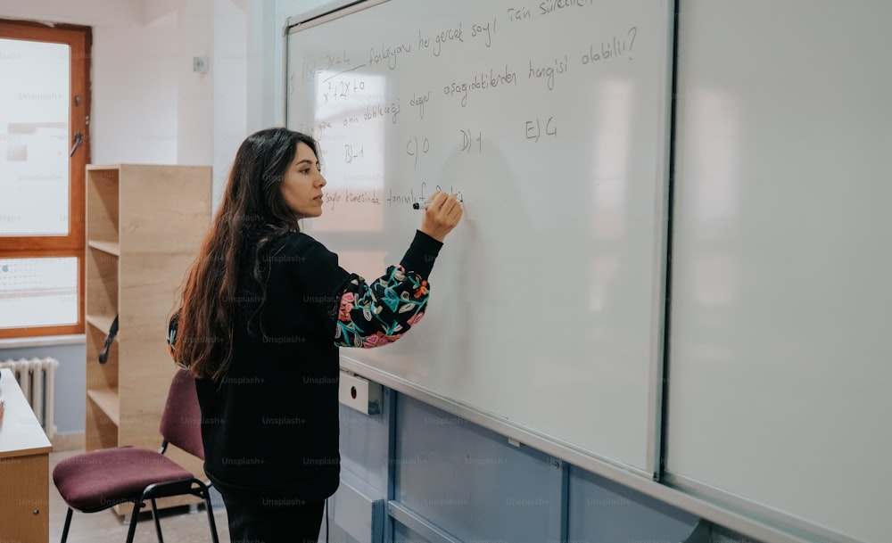 uma mulher escrevendo em um quadro branco em uma sala de aula