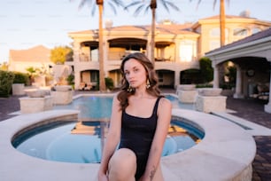 a woman sitting on a ledge next to a pool