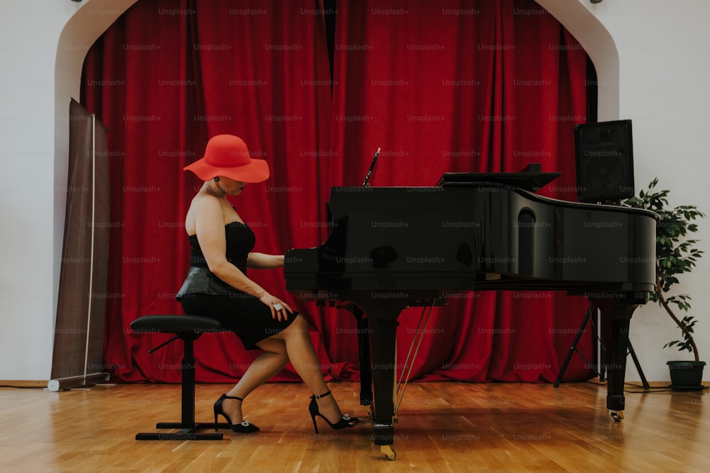 Une femme assise à un piano devant un rideau rouge