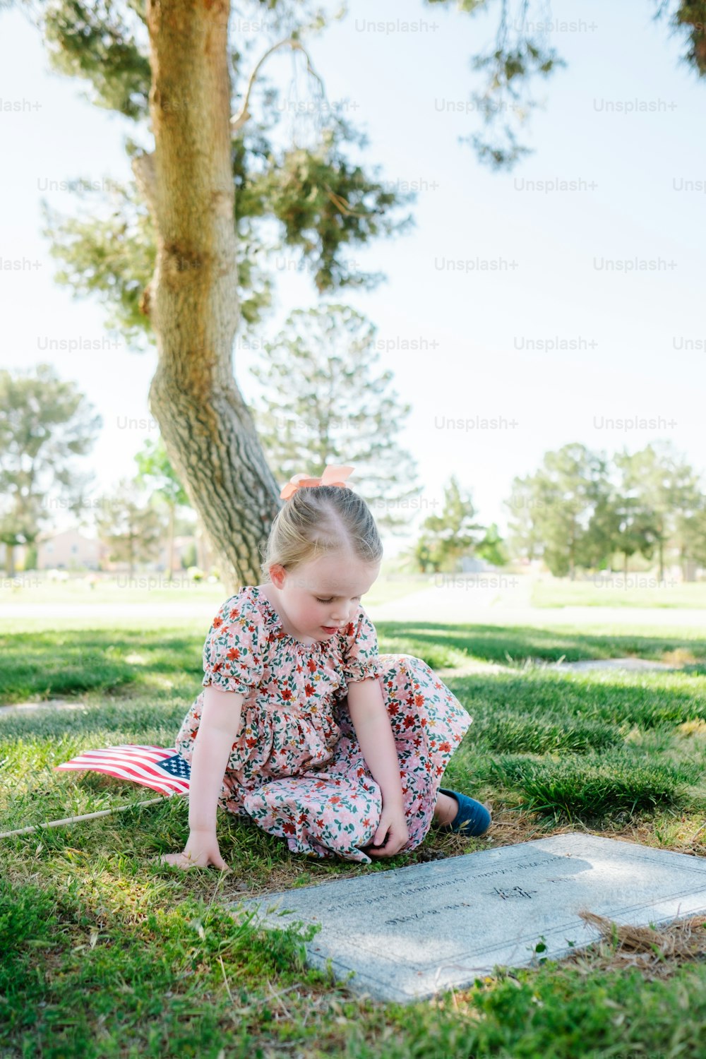 a little girl sitting on the ground next to a tree