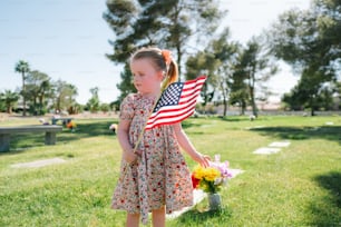 a little girl holding an american flag in a cemetery