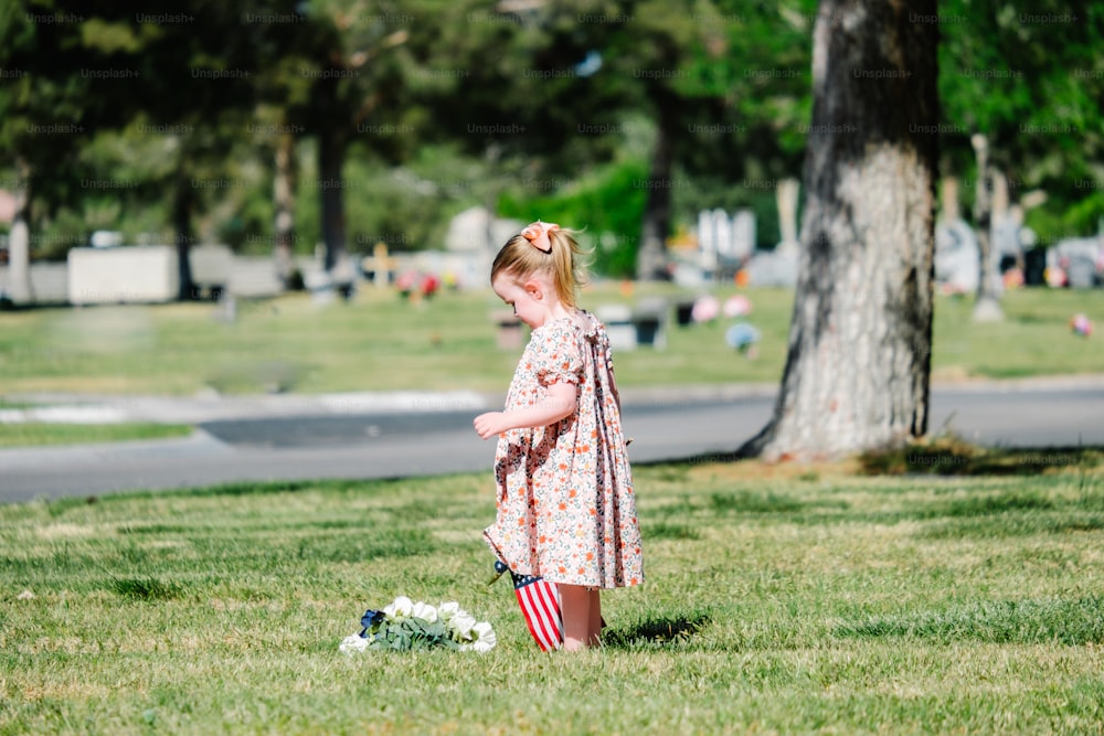 a little girl standing in the grass next to a tree