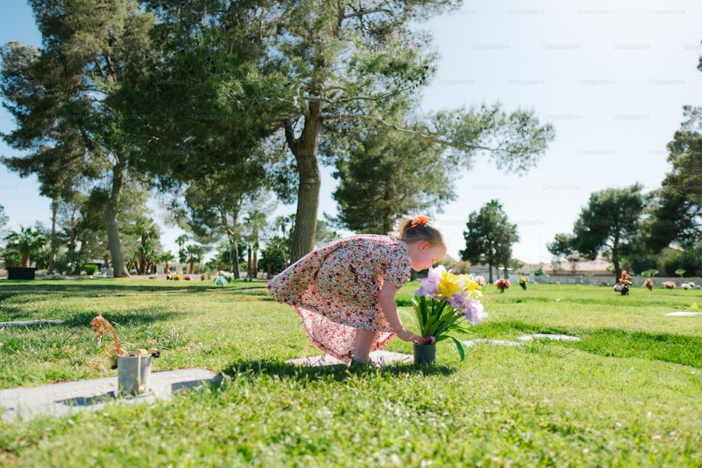 a woman kneeling down to plant flowers in the grass