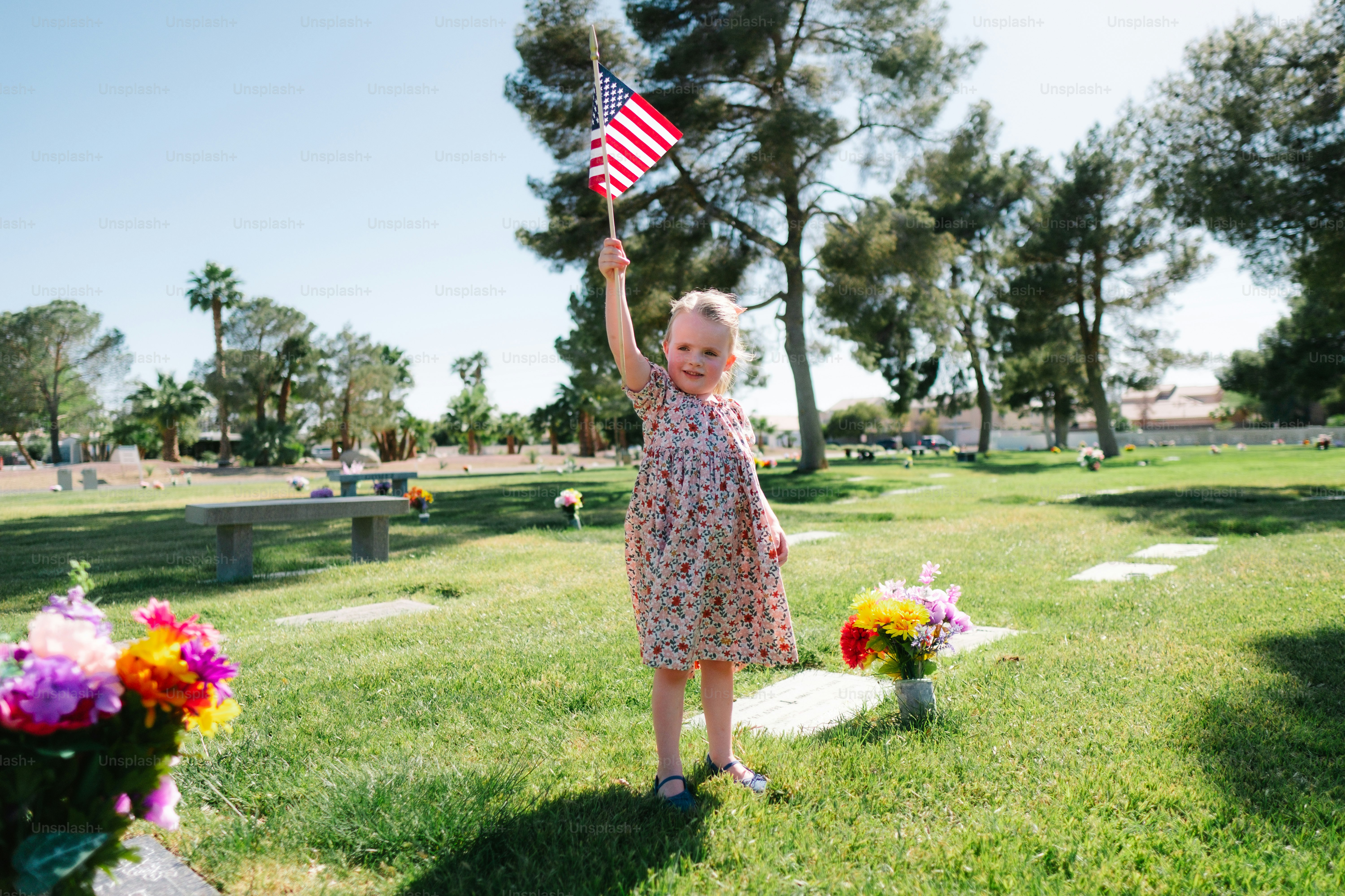 a little girl holding an american flag in a cemetery