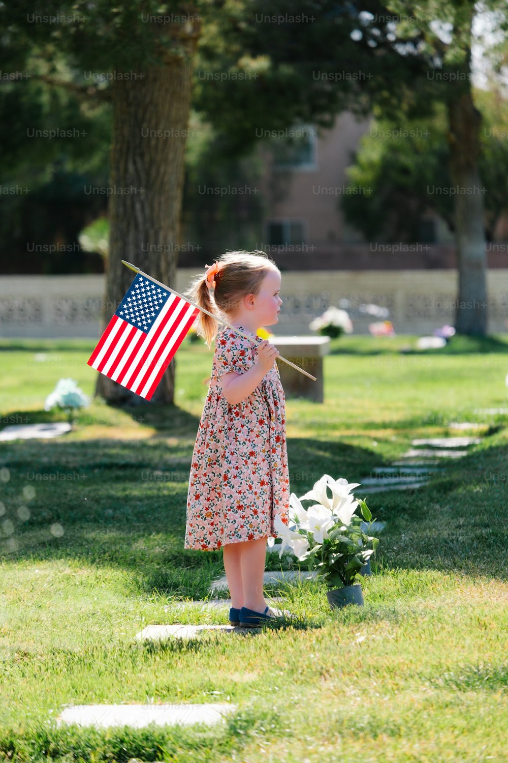 a little girl holding an american flag in a cemetery
