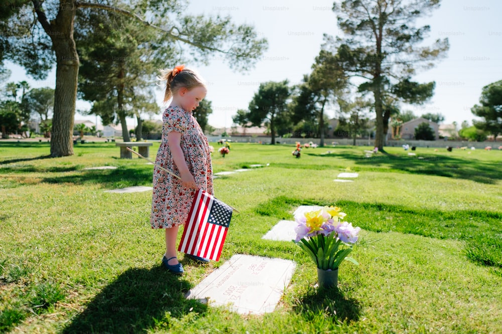 a little girl holding an american flag in a cemetery