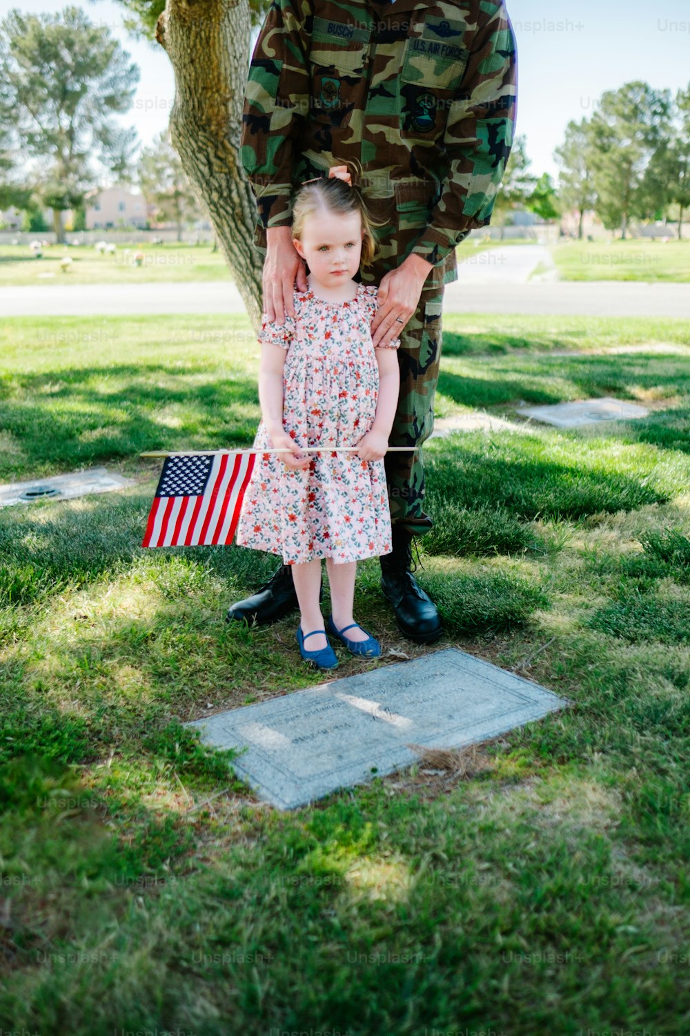 a little girl standing next to a soldier holding an american flag
