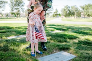 Una niña sosteniendo una bandera estadounidense junto a un soldado