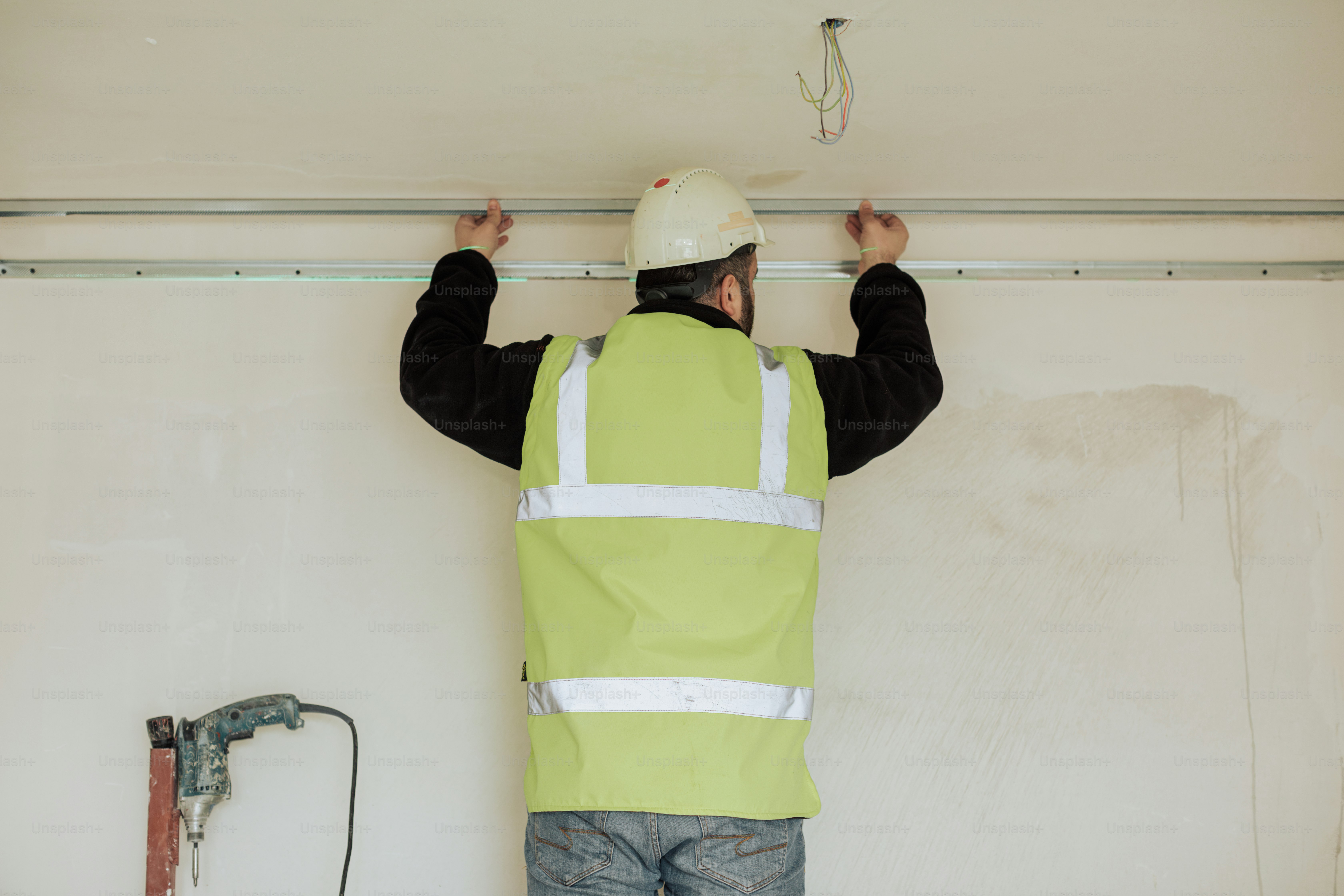 a man in a hard hat and safety vest working on a wall