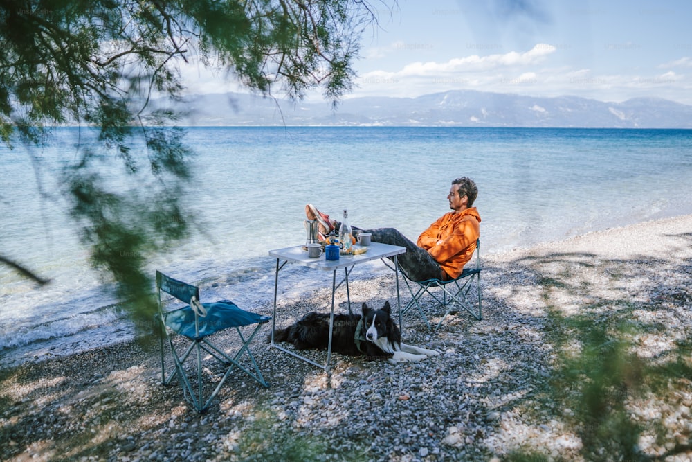 a man sitting at a table next to a dog on a beach