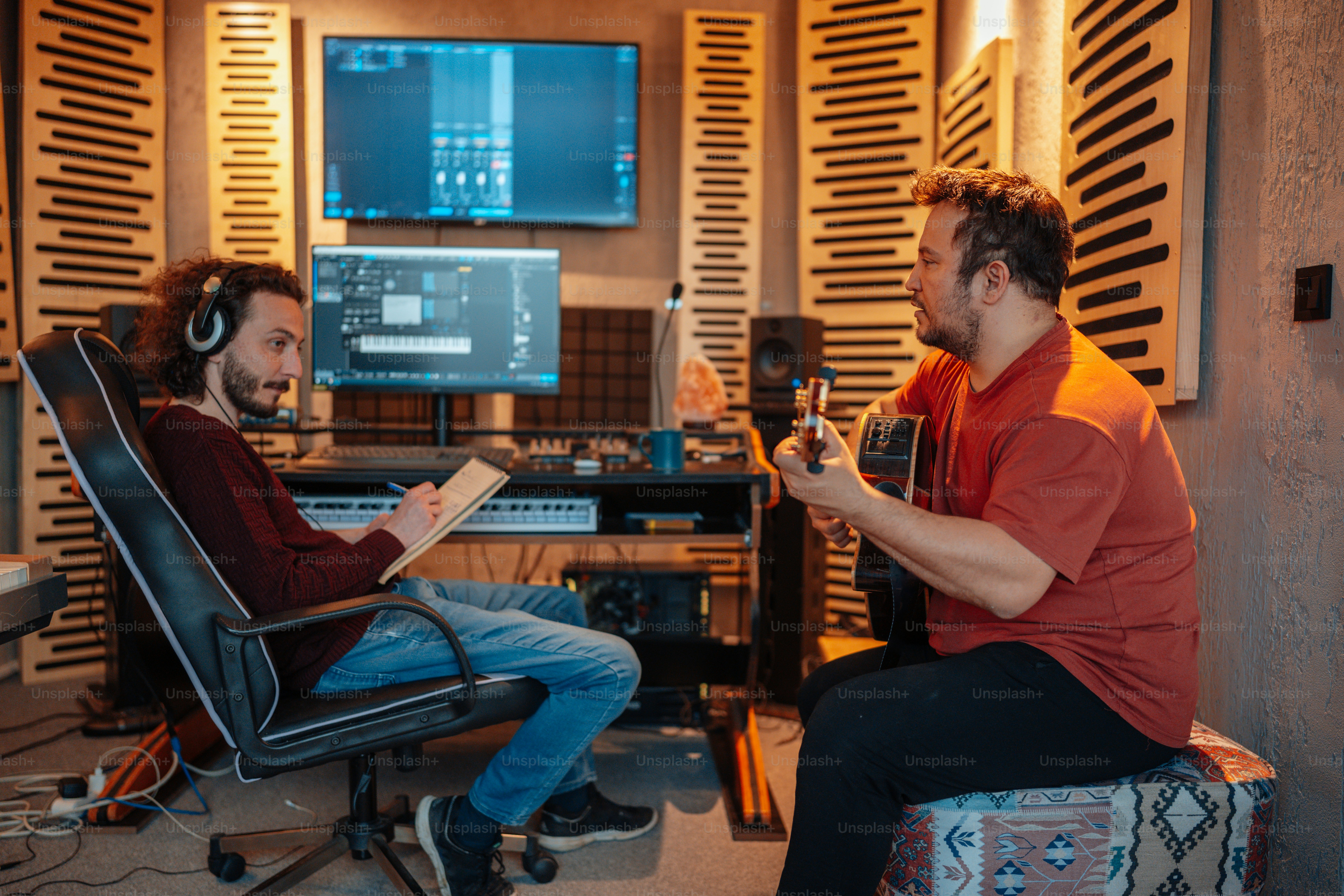 A man sitting in a chair next to another man in a recording studio ...
