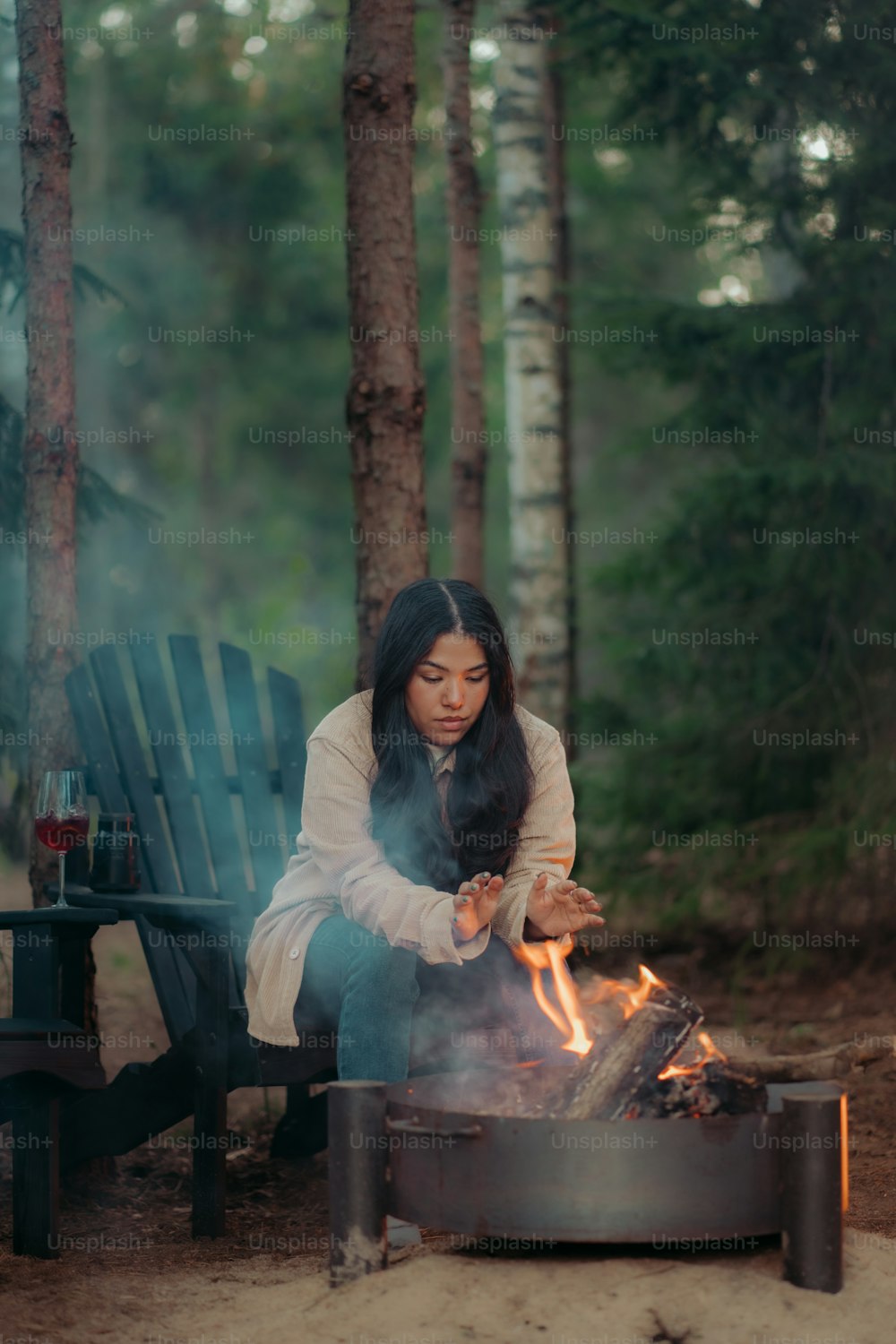 uma mulher sentada em uma cadeira ao lado de uma fogueira