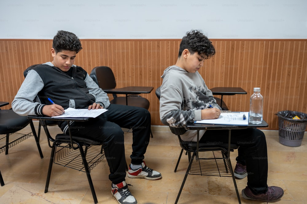 two young men sitting at desks in a classroom