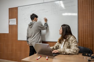 a man standing next to a woman in front of a whiteboard