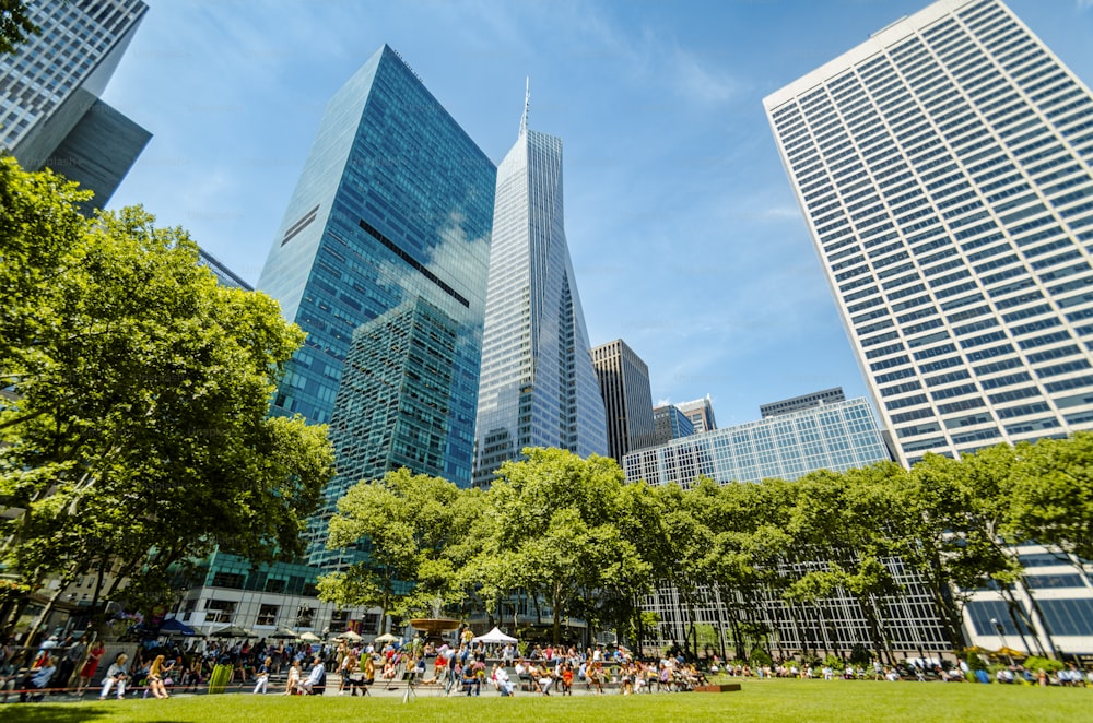 a group of people sitting on a lush green park next to tall buildings