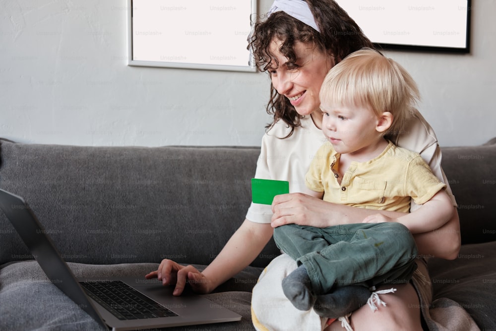 a woman sitting on a couch with a child and a laptop