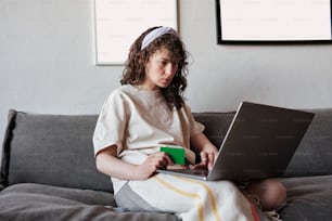 Ein junges Mädchen, das mit einem Laptop auf einer Couch sitzt