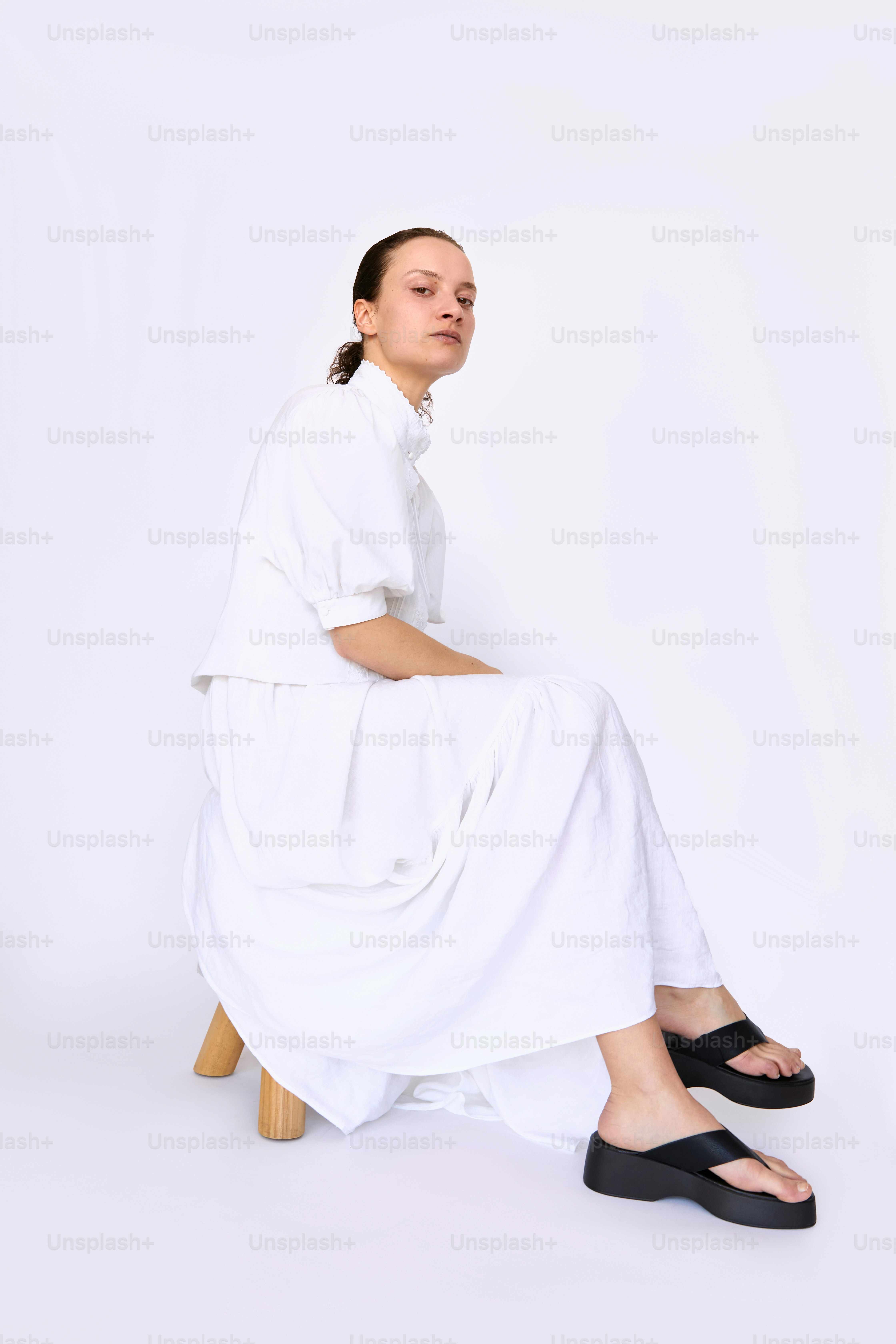 Una mujer con un vestido blanco sentada en un taburete