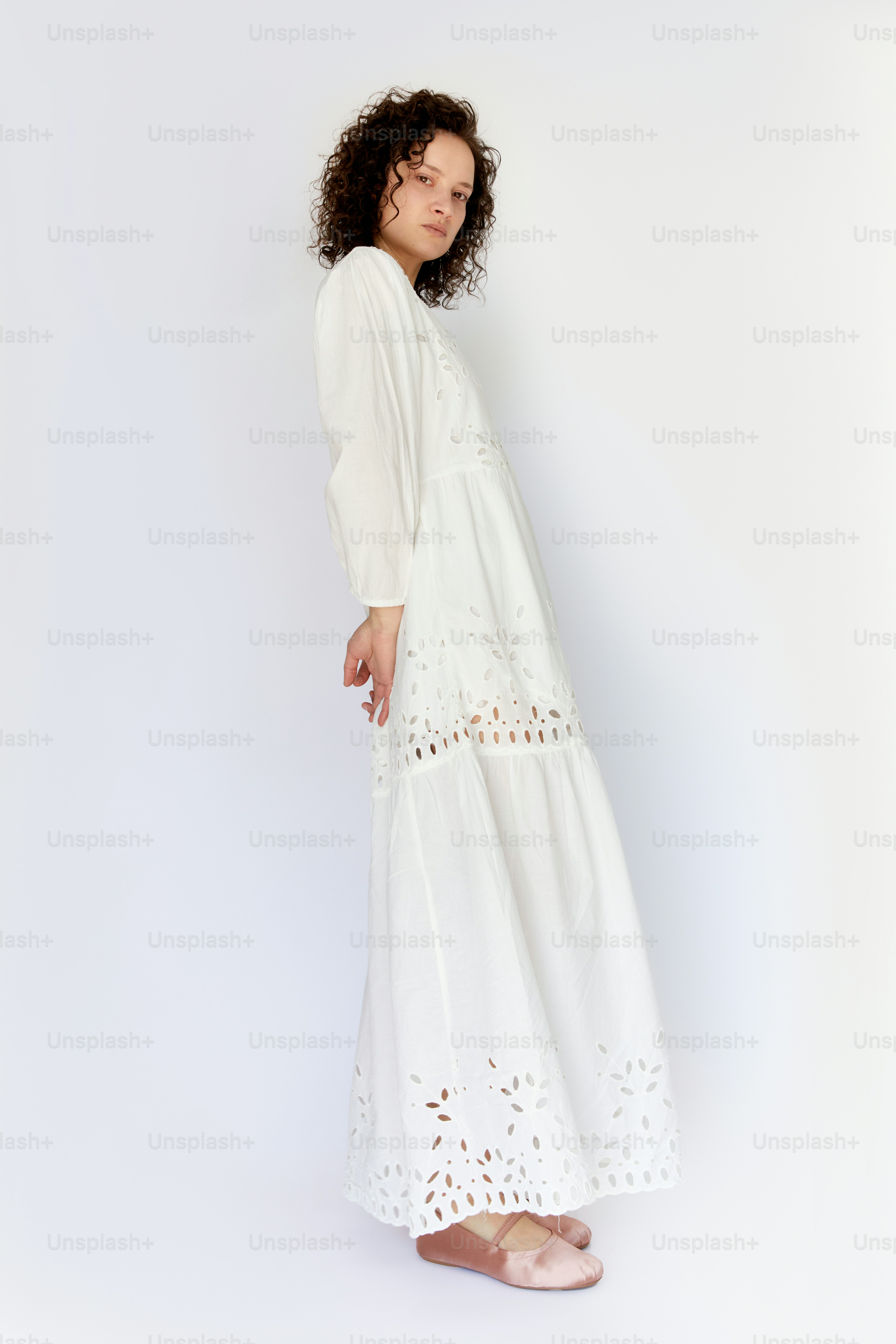 Una donna in un vestito bianco in piedi di fronte a un muro bianco