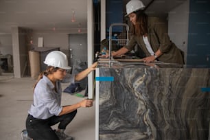 two women in hard hats are working on a wall