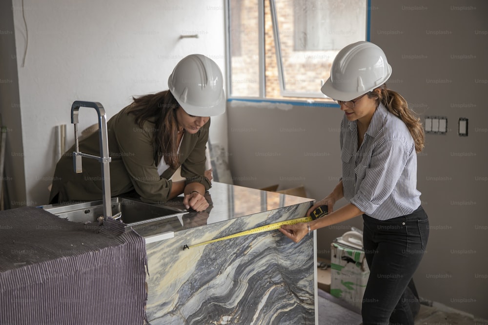 two women in hard hats are working on a wall