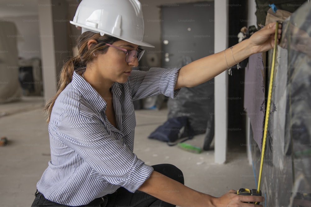 a woman wearing a hard hat and glasses working on a wall