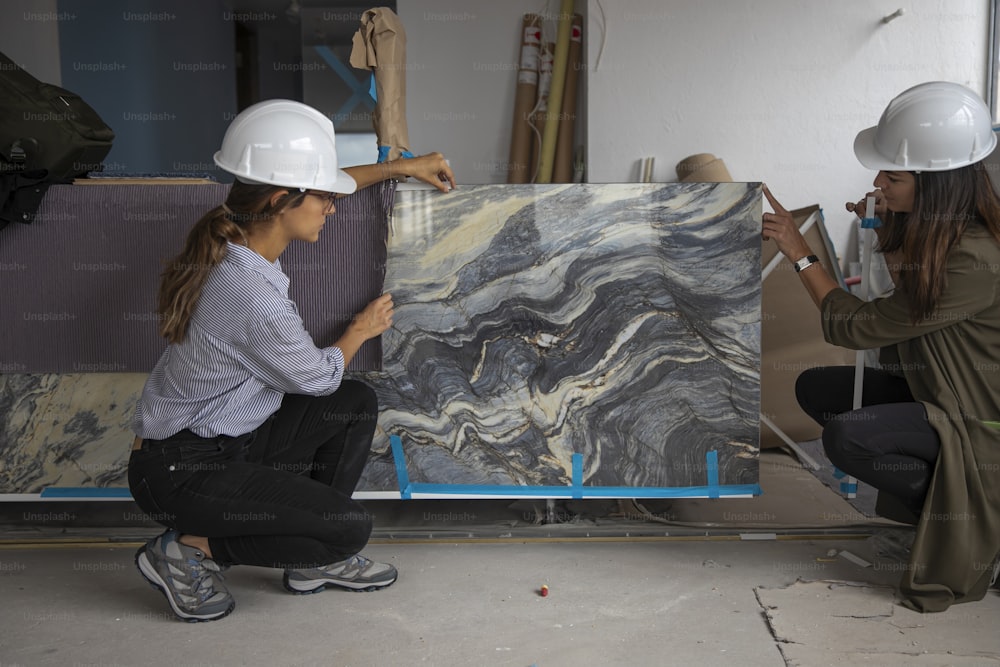two women in hard hats are working on a painting