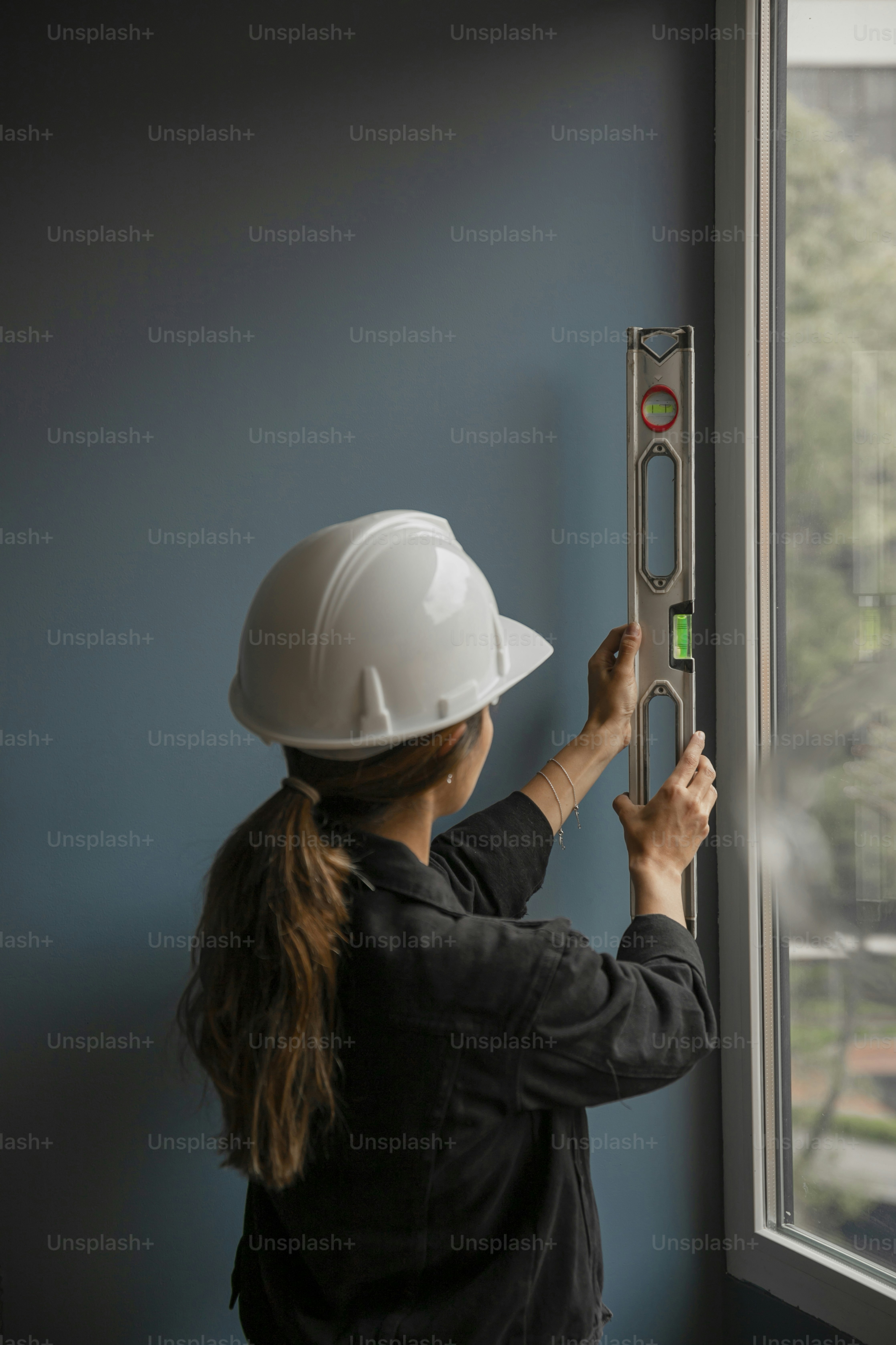 a woman in a hard hat is working on a window