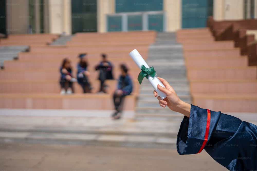 Eine Frau in einem Abschlusskleid hält ein Diplom in der Hand