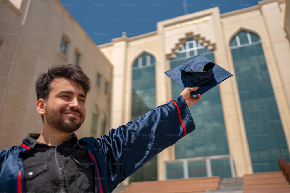 a man holding a graduation cap in front of a building