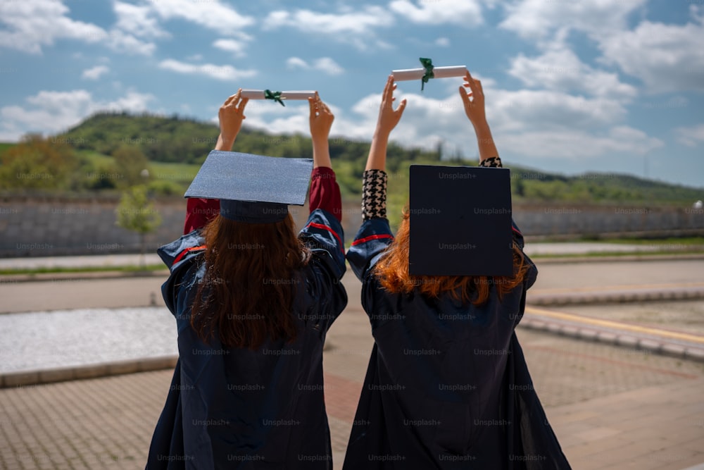 two girls in graduation gowns holding up their hats