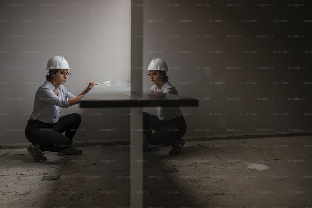 a woman kneeling down next to another woman wearing hard hats