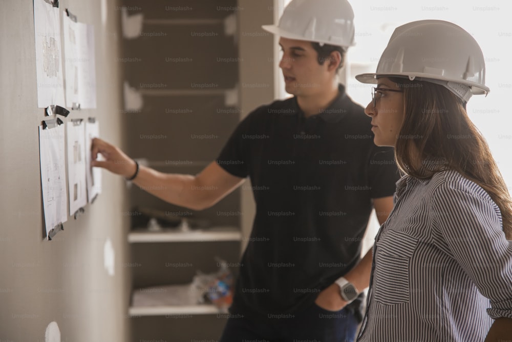 a man and woman wearing hard hats looking at a wall