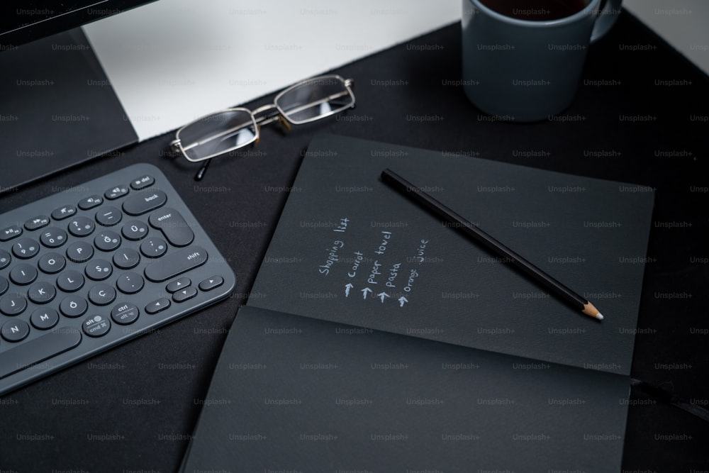ein schwarzer Schreibtisch mit einer Tastatur, einem Notizbuch und einer Tasse Kaffee