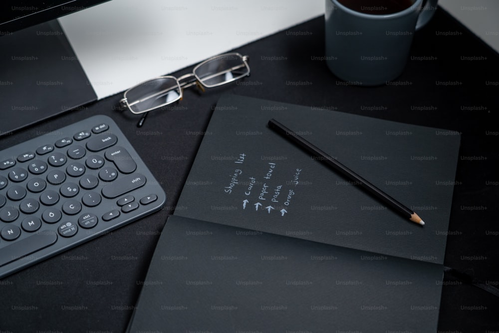 a black desk with a keyboard, notebook and a cup of coffee