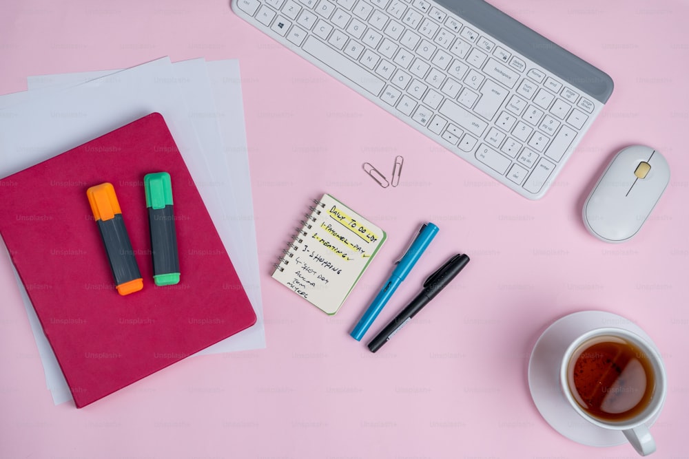 a pink desk with a keyboard, notebook, mouse and a cup of coffee