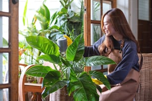Una hermosa joven asiática cuidando y regando plantas de interior regando latas en casa