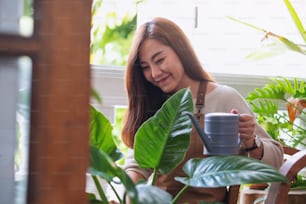 A young woman taking care and watering houseplants by watering can at home