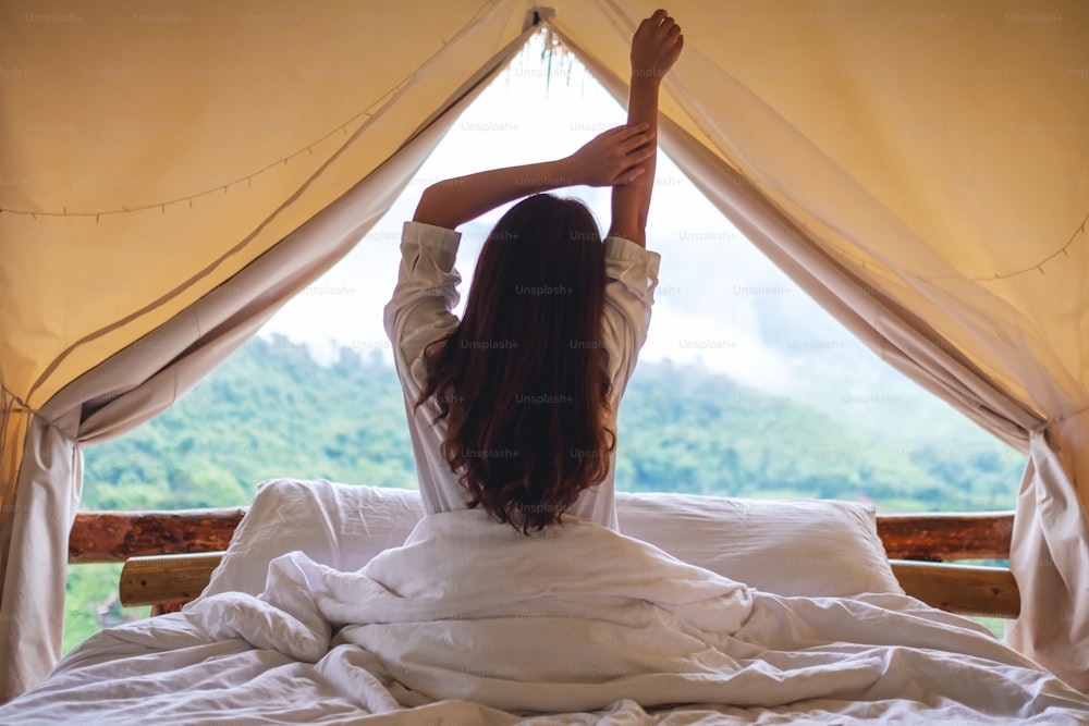 Rear view image of a woman do stretching after waking up in the morning , looking at a beautiful nature view outside the tent