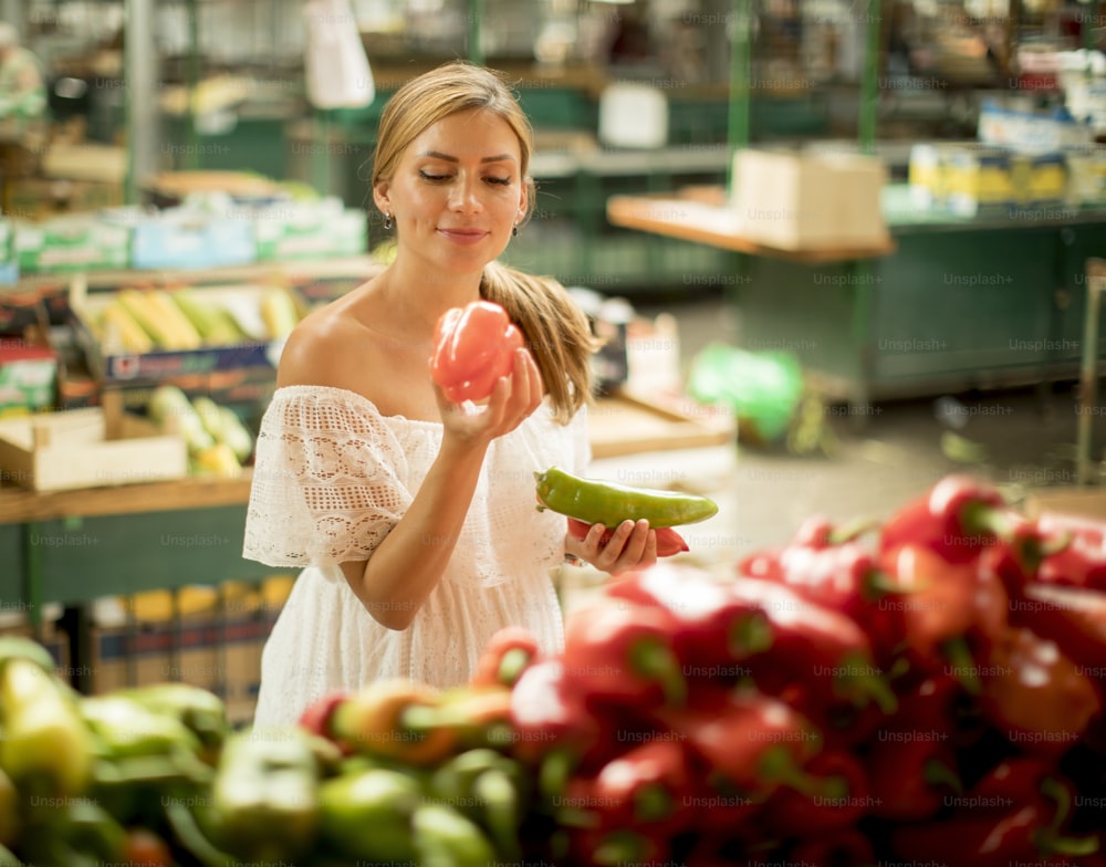 Mujer joven y bonita comprando verduras frescas en el mercado