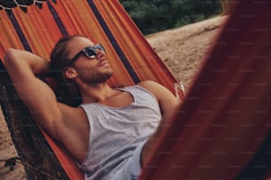 Handsome young man keeping hand behind head while lying in hammock