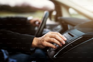 Businessman in suit is adjusting a volume on his stereo while driving a car.