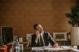 Portrait of senior businessman using mobila phone and working in modern office